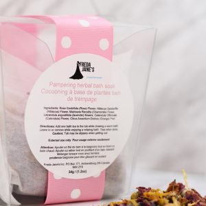 pampering herbal bath in a clear take out container with dry herbs in front with a pink and white dotted ribbon around container