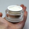 clear jar sitting in palm of hand with white face cream in jar